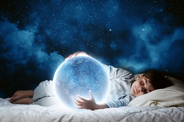 Junge hält im Bett schlafend Mondkugel vor sich